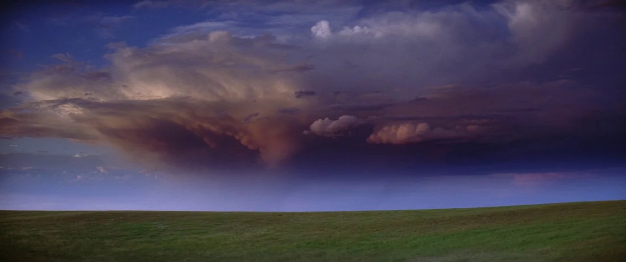 Dances With Wolves (1990) movie still: establishing — A wide, flat field of green grass lies beneath a massive, turbulent storm cloud. The dark…