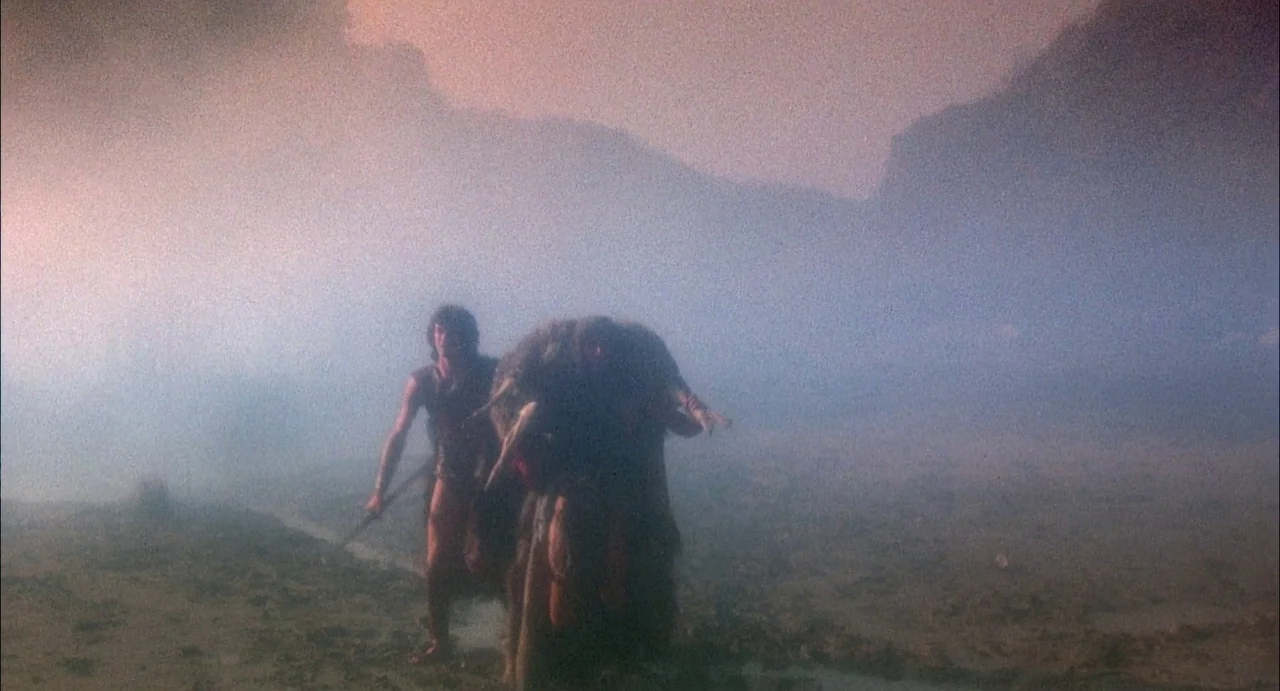 Conquest (1983) movie still: fullbody — A desolate and foggy open landscape with mountainous silhouettes visible in the distance. A man walks…