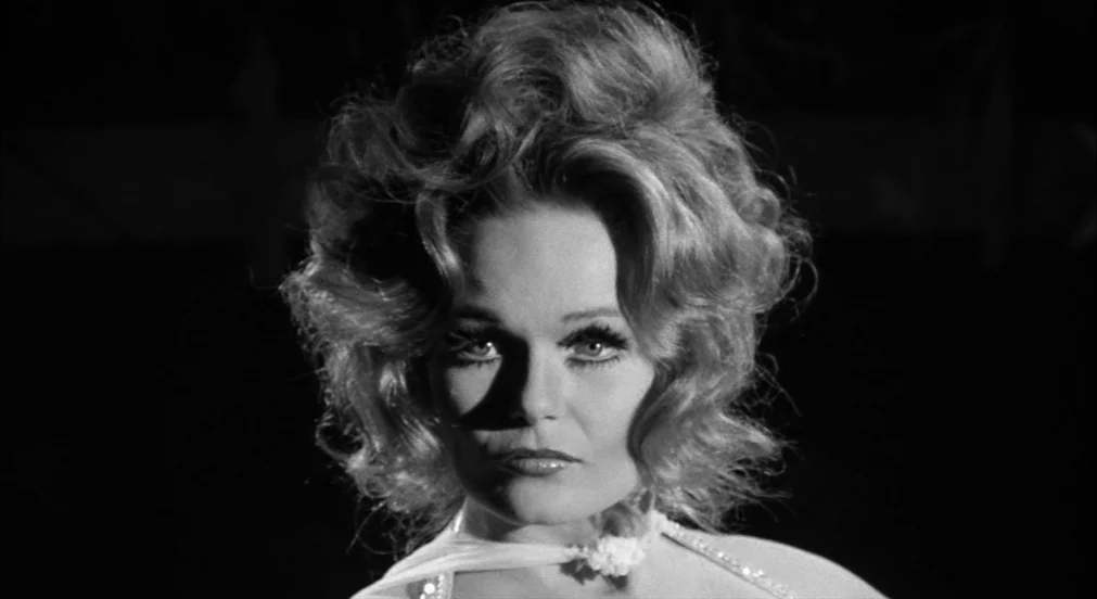 Lenny (1974) movie still: closeup — A dark, empty space frames a woman from the chest up. She looks directly forward under high-contrast stage…