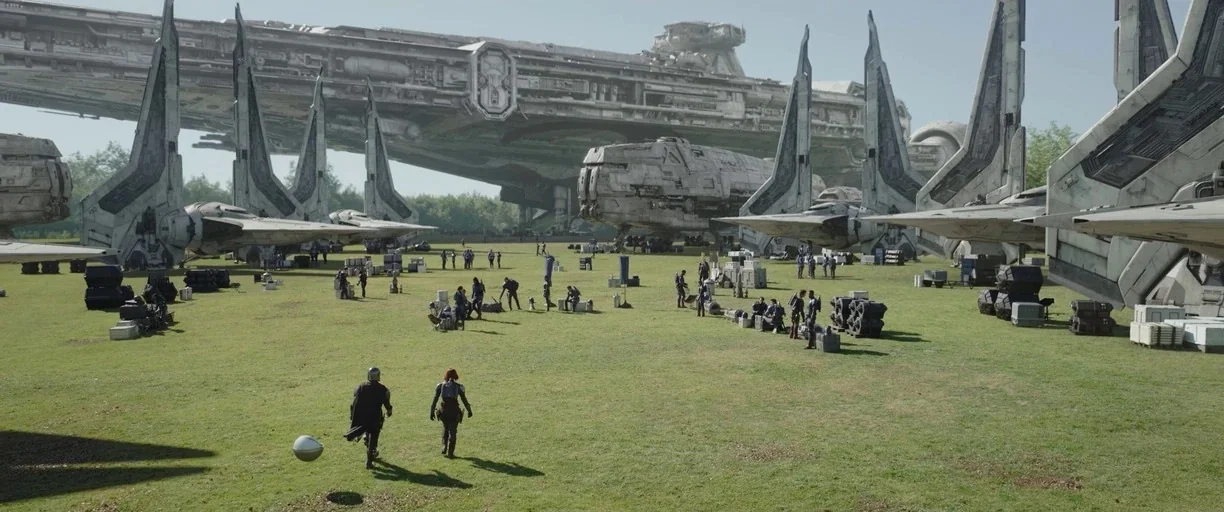 The Mandalorian (2019) movie still: wide — A vast grassy field filled with several large sci-fi spaceships and scattered cargo. Two people walk…