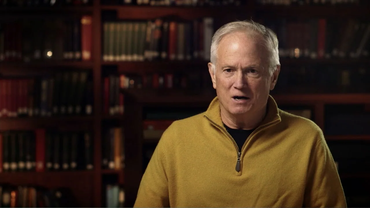 Ali & Cavett: The Tale of the Tapes (2018) movie still: medium — A dark, dimly lit library with rows of blurred books on wooden shelves. An older…