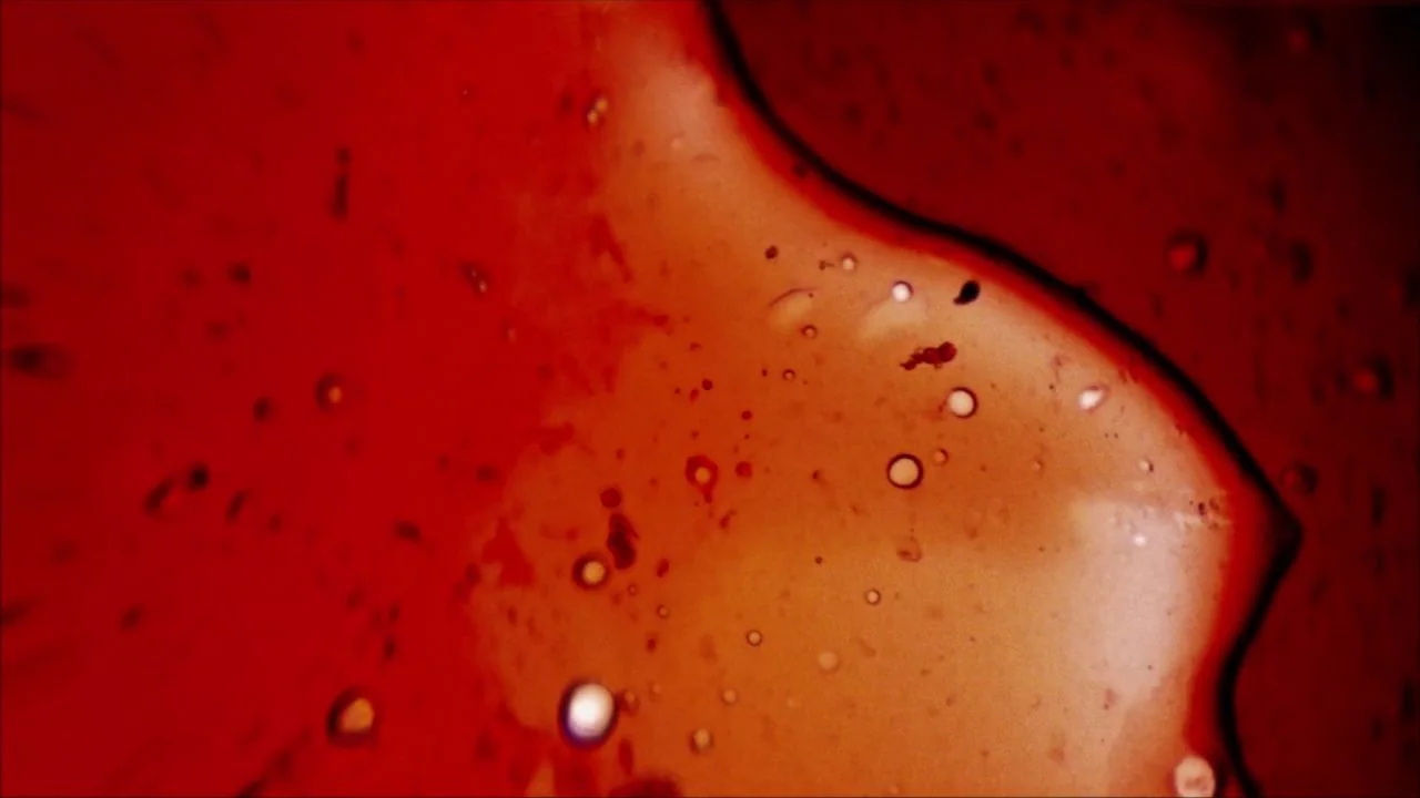 She Dies Tomorrow (2020) movie still: closeup — A close-up view shows swirling viscous red liquid with translucent golden bubbles. Droplets of…