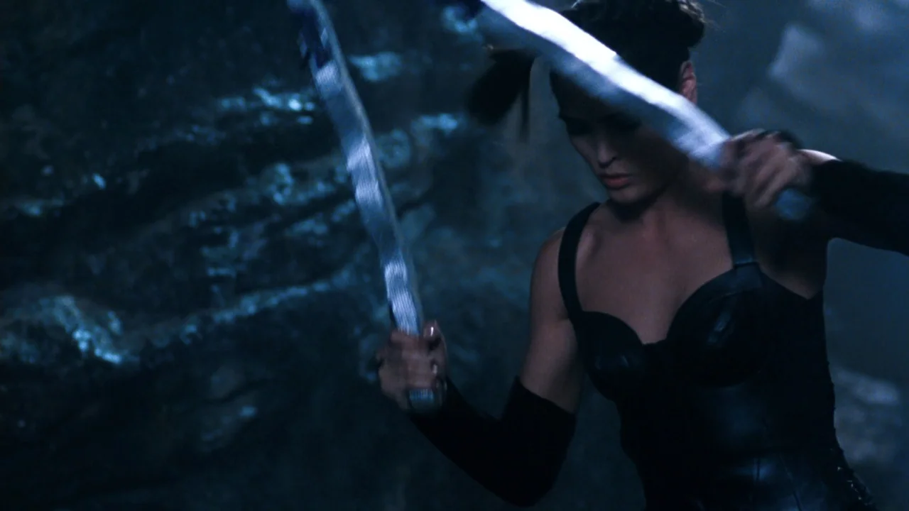 Mortal Kombat: Annihilation (1997) movie still: medium — A dimly lit cavern features craggy rock walls with dark, indistinct shadows. A woman in…