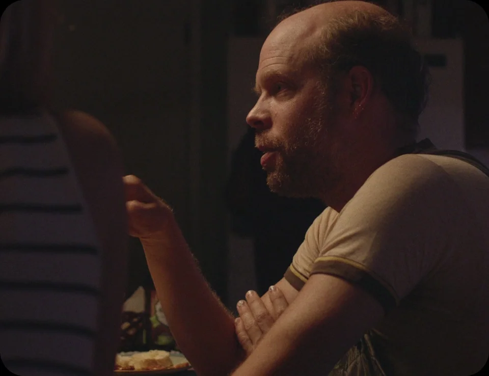 A Ghost Story (2017) movie still: medium — A dark indoor space where two people sit at a table during dinner. The man in the foreground speaks while…