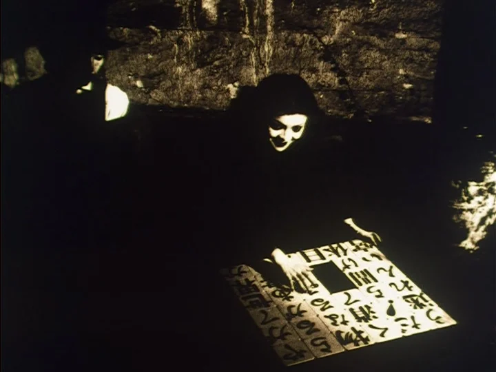 The Reading Machine (1977) movie still: medium — A dark, cavernous space with rough stone walls surrounds the two figures. A woman with pale skin…