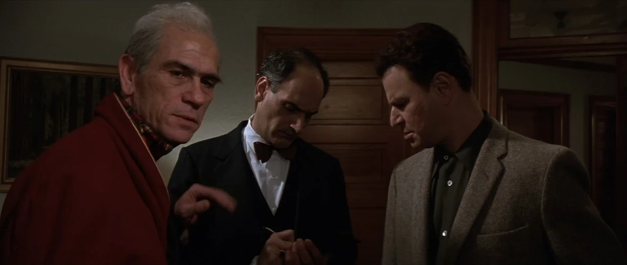 Cobb (1994) movie still: medium — An dimly lit interior space with wooden paneling and minimal decor. Three men stand together in conversation while…