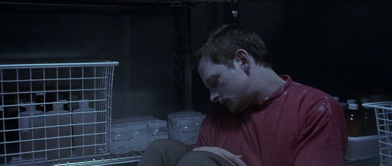 The Frighteners (1996) movie still: medium — A man sits slumped inside a narrow, sterile storage closet filled with plastic containers. He is…