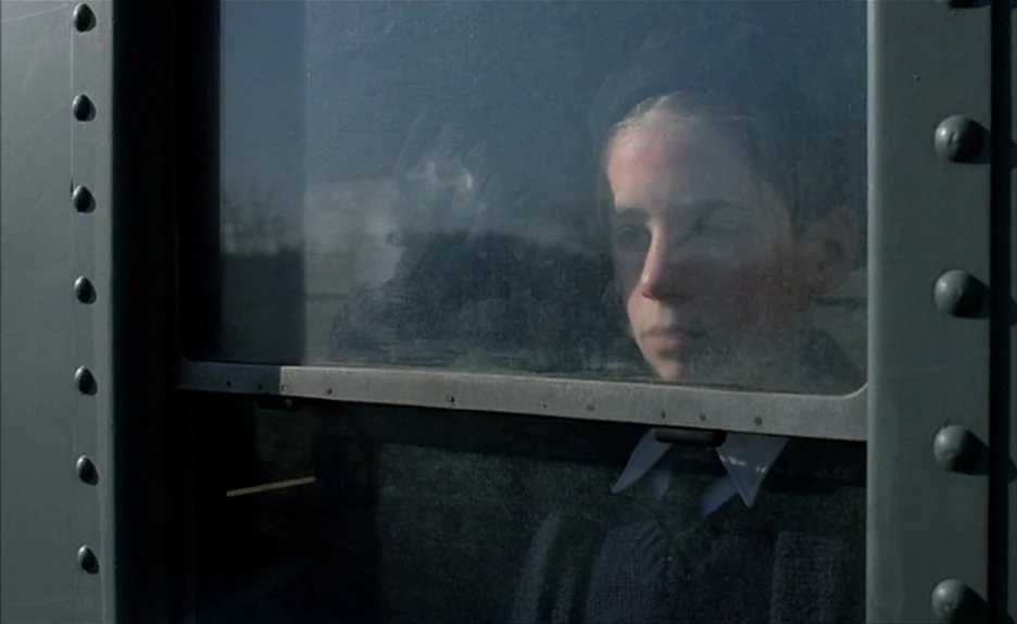 Au Revoir Les Enfants (1987) movie still: closeup — A young boy sits behind a metal-framed glass window on a train. He looks out the glass pane…