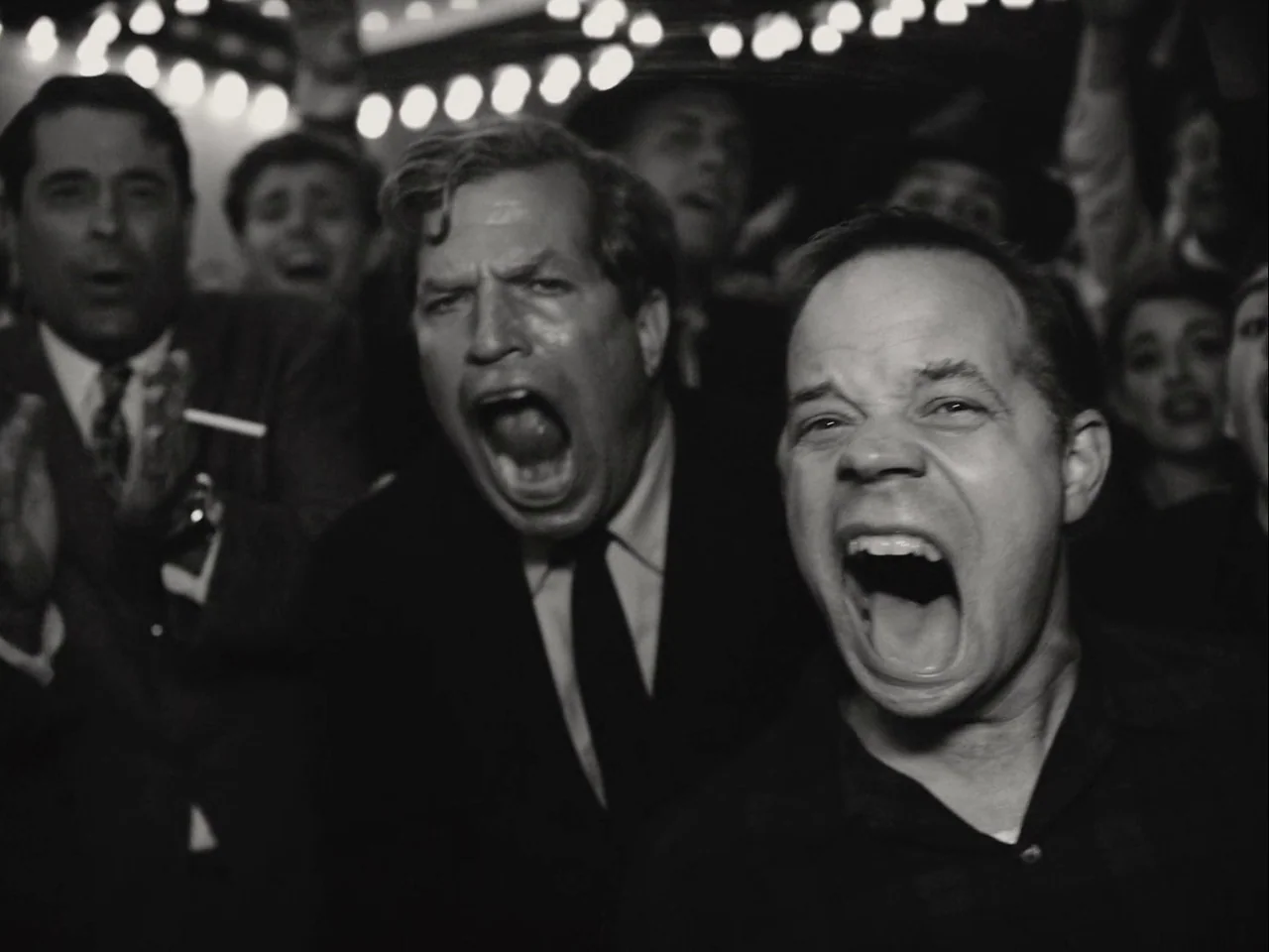 Blonde (2022) movie still: medium — A dense crowd of people at night under bright stadium or theater lights. Multiple men in suits yell excitedly…
