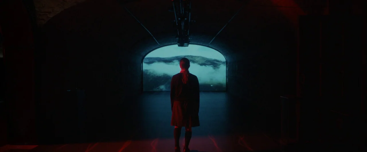 You Are Not My Mother (2021) movie still: fullbody — A dark, vaulted concrete room features a large projection screen displaying a mountain…