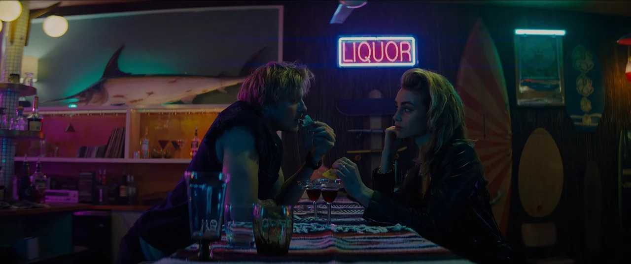 Night Teeth (2021) movie still: medium — A dimly lit home bar decorated with surfboards and a large mounted marlin. A young man and woman face each…
