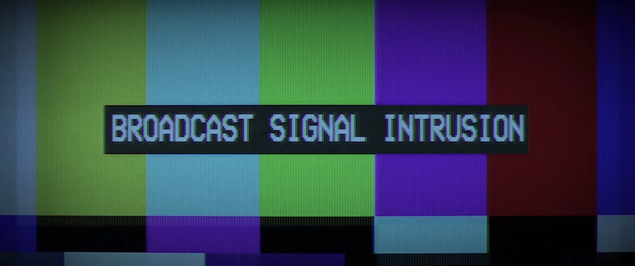 Broadcast Signal Intrusion (2021) movie still: closeup — A television screen displays a standard SMPTE color bars test pattern. White sans-serif…