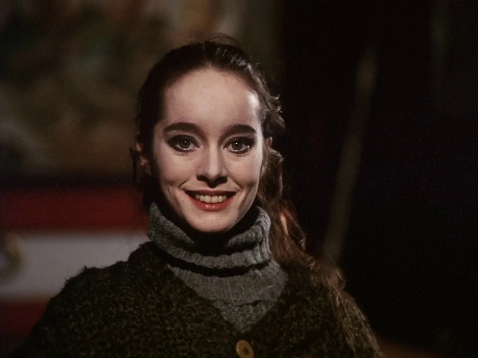The Clowns (1970) movie still: closeup — A woman stands in a dim indoor space with an out-of-focus background. She gazes directly at the lens with a…