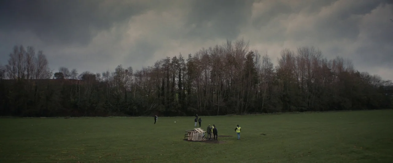 You Are Not My Mother (2021) movie still: wide — A wide, open green field is bordered by a line of leafless autumn trees. A small group of people…