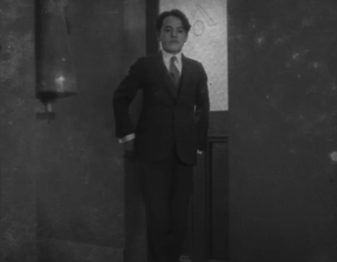 Tokyo Chorus (1931) movie still: fullbody — A man stands centered within a simple wooden framed doorway in a dimly lit room. He is positioned facing…