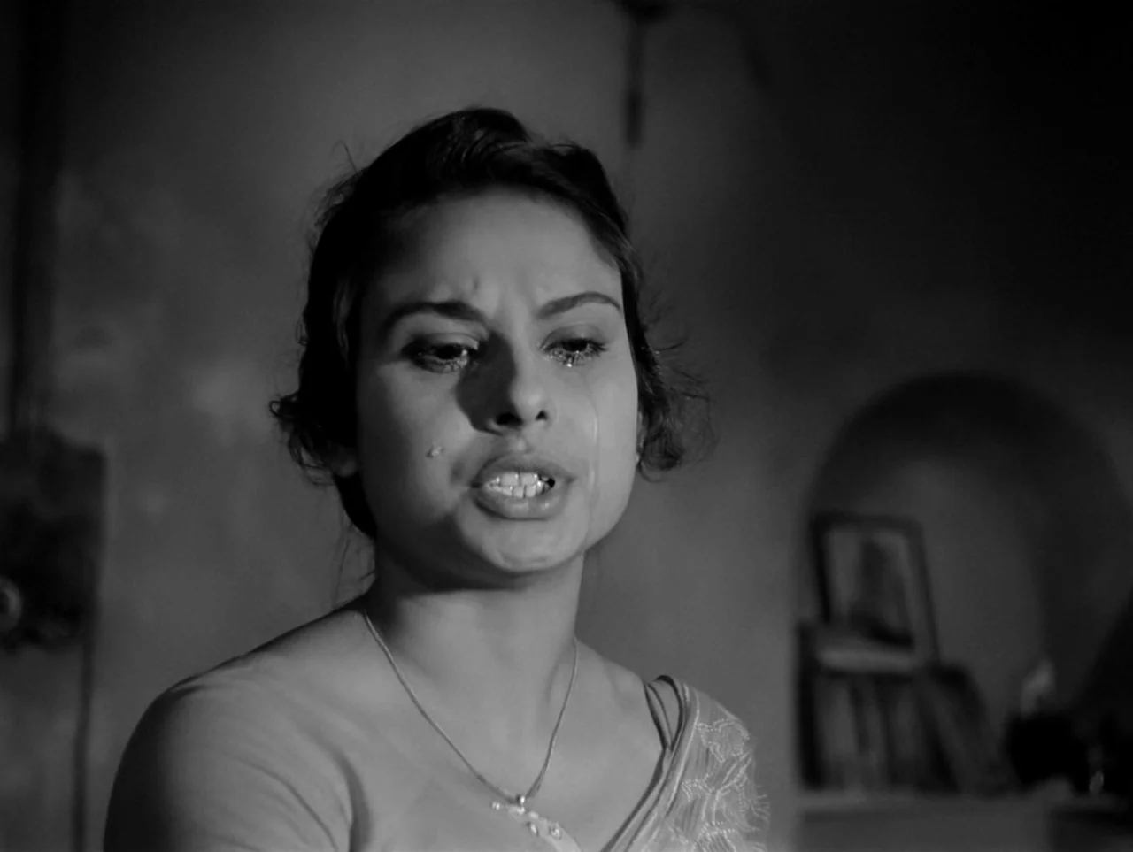 The Coward (1965) movie still: closeup — A dimly lit interior space features a dark arched wall niche in the background. A young woman cries while…